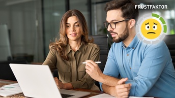 Zwei vielbeschäftigte Kollegen unterhalten sich im Büro, während sie vor dem Laptop sitzen.