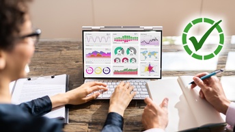 Zwei Menschen sitzen vor einem Laptop, das ein Statistik-Dashboard zeigt