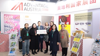 Porträt von sieben Personen, die nebeneinander neben verschiedenen Ständern mit Prospekten stehen. Zwei der Personen halten ein Schild, auf dem go international steht. Hinter ihnen ist eine Wand, auf der Advantage Austria steht