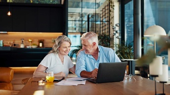 Ein Paar sitzt an einem Tisch und liest an einem Laptop