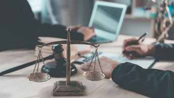 Waage der Gerechtigkeit vor zwei Menschen, die an Unterlagen arbeiten
