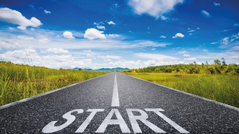Weißer Schriftzug Start auf langer Straße mit grünem Feld und blauem Himmel<br />
