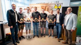 5 Lehrlinge mit Preisen in den Händen posieren neben 3 Herren in einem Raum