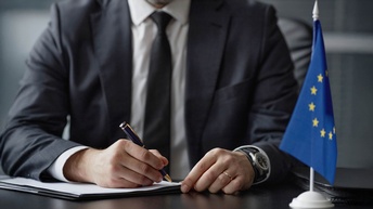 Ein Mann schreibt auf Papieren - daneben die Flagge der EU