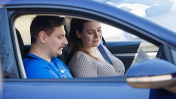 Fahrlehrer mit Fahrschülerin in einem blauen Auto