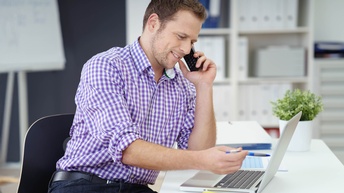 Ein freundlicher Mann im Büro am Laptop telefoniert