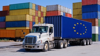 Containerstapel im Hintergrund. Vorne ein LKW mit der Flagge der EU