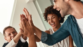 Geschäftsleute, die sich gegenseitig abklatschen und lächeln, während sie in einem modernen Büro zusammenarbeiten<br />
