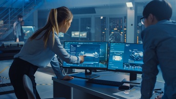 Personen in Rückenansicht in dunklem Raum mit bläulichem Licht blicken auf Monitore, auf denen Renderings von Automobilen zu sehen sind