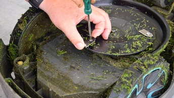 Nahaufnahme einer Hand, die an der Unterseite eines Mähroboters rumschraubt