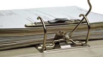 Ein Stapel Blätter in einem Ordner - der Hebelmechanismus zum Zusammenhalten der Papiere im Vordergrund