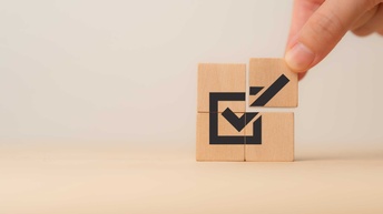 vier Holzklötzchen bilden aufeinandergesetzt eine angehakte Check-Box