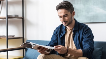 Junger Mann sitzt auf einem Sofa und liest eine Zeitschrift