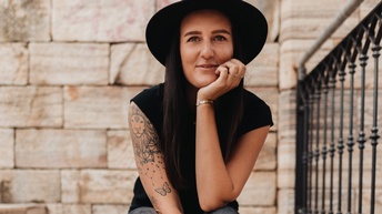 Eine junge Frau mit Hut sitzt auf Freitreppen, das Kinn in die Hand gestützt