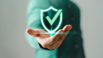 Im Vordergrund ist die Grafik eines grünen Hakens. Darunter ist die Hand einer Person