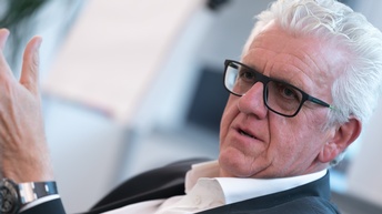 älterer Herr mit schwarzer Brille und im Anzug ist in einer Diskussion und gestikuliert