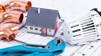 kleines Haus auf Bauplan mit Heizungsregler und Rohren