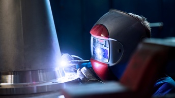 Ein Mann mit Schweißermaske schweißt an einem konischen Metallteil