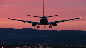 Flugzeug in Rückansicht bei Landung auf beleuchtete Landebahn im Abendrot