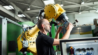 Ein Mann justiert einen Roboterarm in einer Werkhalle