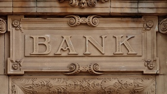 Detailansicht eines historischen braungrauen Türgiebels mit Stuckaturelementen, mittig im Fokus Schriftzug Bank