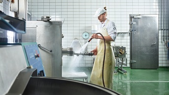Person reinigt Maschinen in einem Fleischereibetrieb