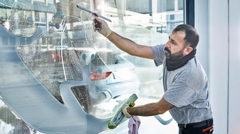 Ein Mann reinigt eine große Fensterfront von außen mit einem Abzieher. Auf die Fensterscheibe ist eine Echse aufgedruckt