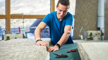 Ein junger Mann bespannt ein noch zerlegtes Möbelstück mit Stoff