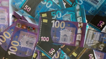 Detailansicht mehrerer Euro-Banknoten auf einem Haufen, farblich ins Negativ invertiert