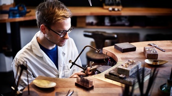 Ein junger Mann sägt in der Werkstatt an einem Goldring