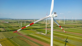 Fokus auf Windrad mit rotweißroten Spitzen auf Feld mit weiteren Windrändern stehend unter blauem Himmel