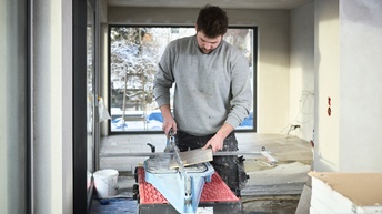 Ein Mann schneidet eine graue Fliese an einem Fliesenschneidegerät. 