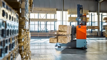 Industriehalle mit Regalen voller Holzbretter, in der Mitte Gefährt beladen mit weiteren Holzbretterstapeln