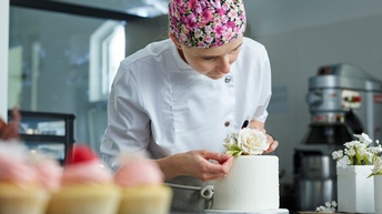 Eine junge Konditorin schmückt einen kleinen Kuchen mit einer Rose aus Zuckerzeug