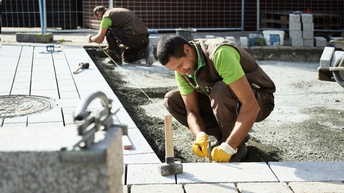 Zwei Männer pflastern einen Straße mit Steinen. Zuerst spannen sie eine Schnur zur Orientierung