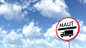 Vor einem blauen Himmel mit weißen Wolken ist in der rechten Bildhälfte eine vertikale Metallstange, auf der ein Schild angebracht ist. Auf dem Schild steht Maut, darunter ist ein schwarzer Strich, darunter ist ein LKW