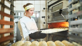 Eine junge Konditorin holt ein Blech frisches Baiser aus dem Ofen