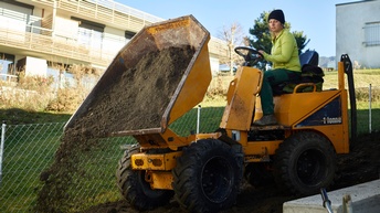 Eine junge Landschaftsgärtnerin schüttet mit dem Schaufelbagger Erde auf