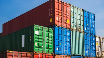 Viele Container in unterschiedlichen Farben stehen in mehreren Stapeln nebeneinander unter blauem Himmel.