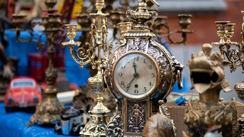 Fokus auf eine antikeUhr, daneben und dahinter stehen weitere verschiedene Altwaren auf einem Tisch