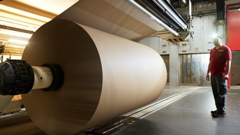 Person mit Kopfleuchte steht vor großer Maschine mit Papierrolle