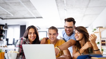Gruppe von jungen Erwachsenen blickt freudig auf einem Laptopbildschirm in einer modernen Büroräumlichkeit