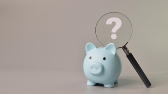 Ein blaues Sparschwein vor einem grauen Hintergrund sowie eine Lupe mit einem weißen Fragezeichen