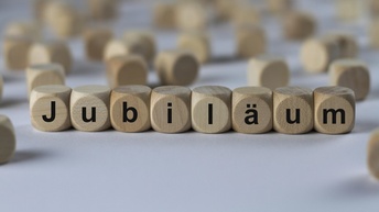 Jubiläum, Holzwürfel mit Buchstaben im Vordergrund, in der Unschärfe verschwommen noch weitere Würfel ohne Buchstaben