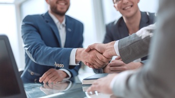 Händeschütteln im Fokus, zwei Personen im Anzug lächeln Hand gebende Person an