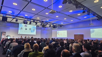 Personen in einem Vortragsaal im Zuge der Veranstaltung STROM DAYS von Startup-Now. Die Personen sitzen auf Sesseln, man sieht außerdem einen Bildschirm mit einer Präsentation. 