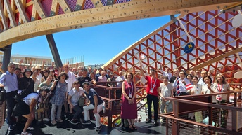 Großes Gruppenfoto von vielen Personen, die im Freien bei einem Pavillon stehen und lächeln. Manche der Personen haben Ausweisschilder um den Hals. Manche halten rot-weiß-rote Flaggen