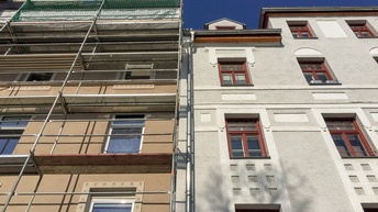 Die Fassaden zweier Altbaugebäude direkt nebeneinander. Vor der Fassade des linken Hauses ist ein Baugerüst. Über den Gebäuden ist der blaue Himmel