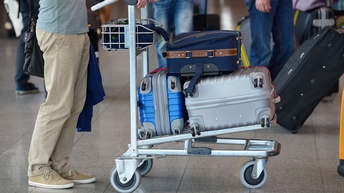 Eine Person schiebt einen Gepäcktrolly voll mit Koffern