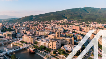 Stadtansicht Skopje: Blick von oben auf die Stadt mit historischen Gebäuden und Monumenten, Fluss Vardar mit Brücken dre Hauptstadt von Mazedonien unter blauem Himmel. Im Hintergrund sieht man eine begrünte hügelige Landschaft, den Berg Vodno.